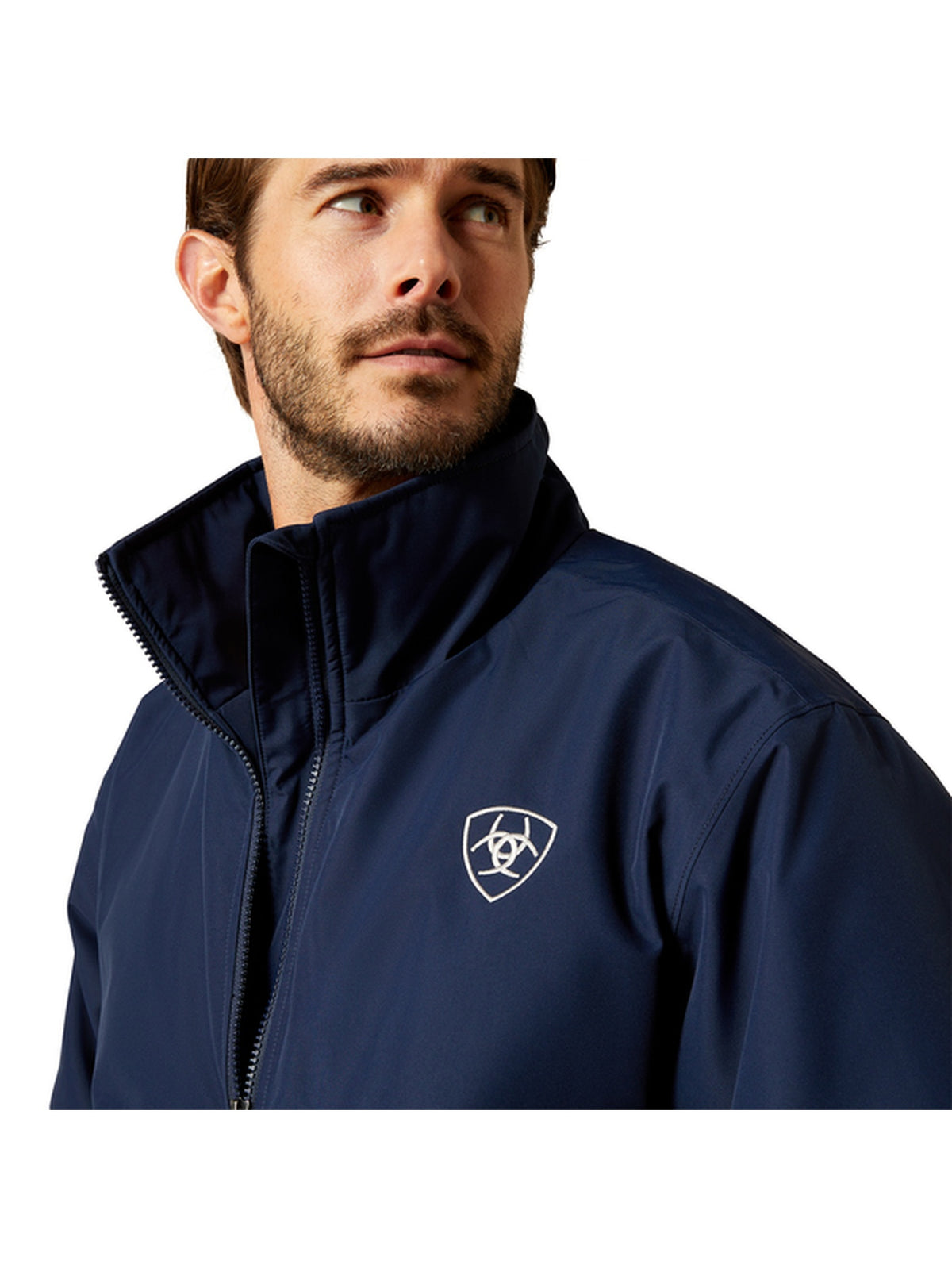 A man wearing a navy blue zip-up jacket with a high collar and a white shield logo on the left chest, shown against a plain white background.