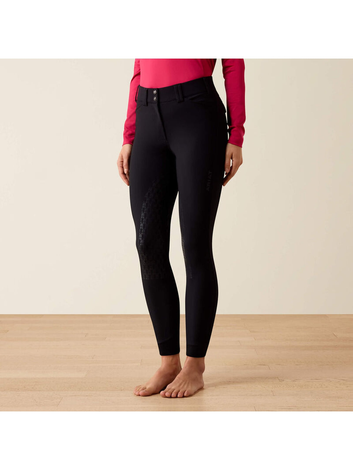 Black equestrian riding breeches with textured knit leg panels, modeled on a person wearing a pink long-sleeve top against a beige studio background.